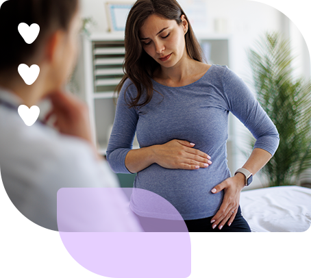 A young pregnant woman gently holding her belly with both hands, looking down with a caring and thoughtful expression.